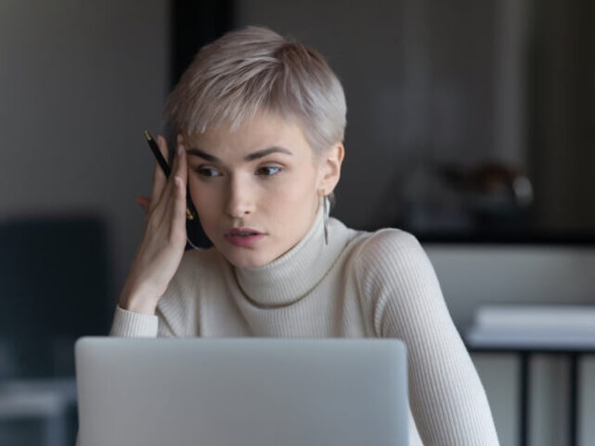 Serious short hired business woman sit in front of laptop considering decision she looking