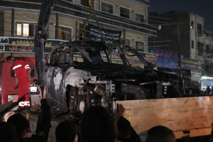 People watch as a vehicle that was hit by a deadly drone strike is removed from a Baghdad