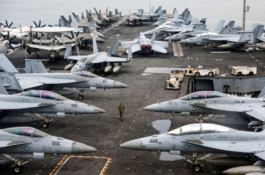 A US Navy officer walks past fighter jets parked on the flight deck of the USS Abraham air