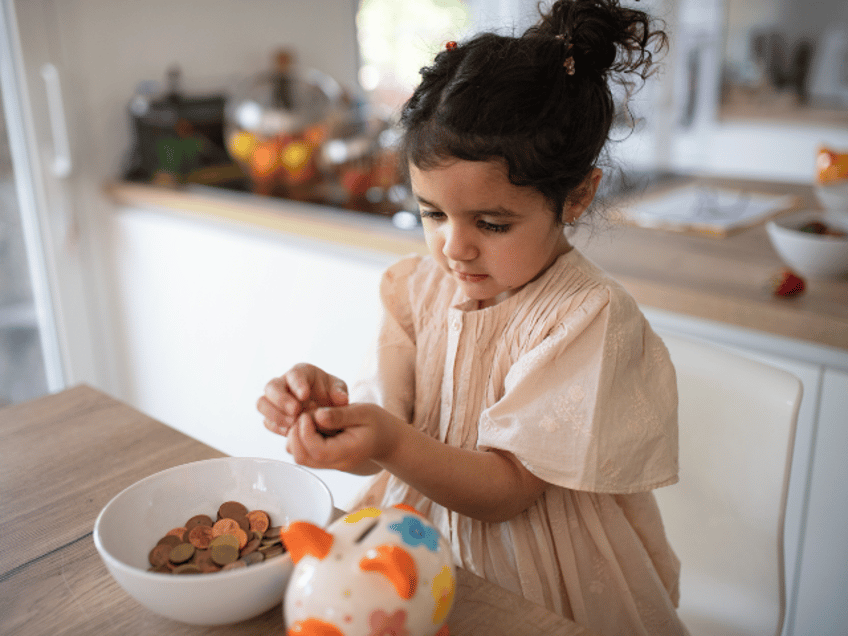 Little multiracial girl saving her money in to porcelain pig.
