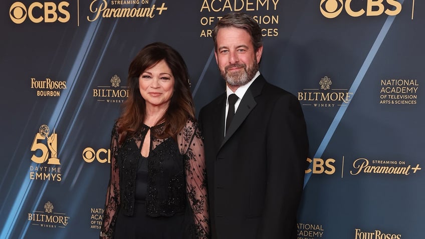 Valerie Bertinelli in a lace long sleeve black dress soft smiles on the carpet with boyfriend Mike Goodnough in a black suit