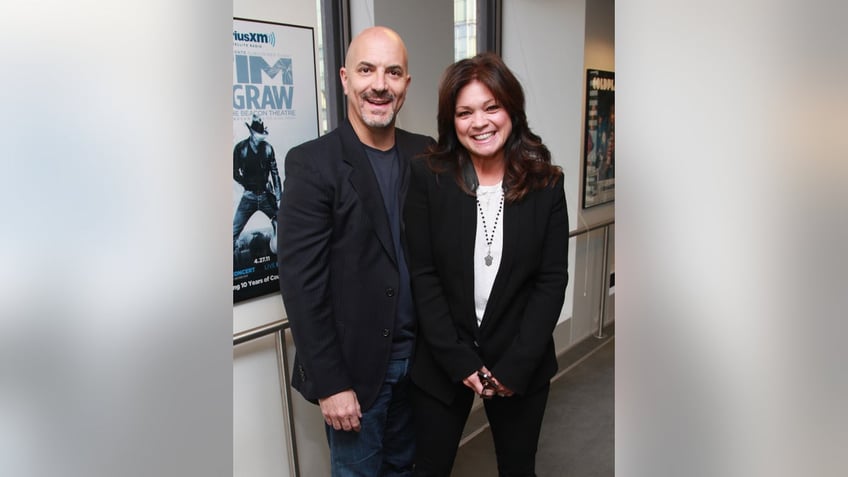 Tom Vitale in a black shirt and suit and Valerie Bertinelli in a white shirt and black suit pose for a photo together in New York