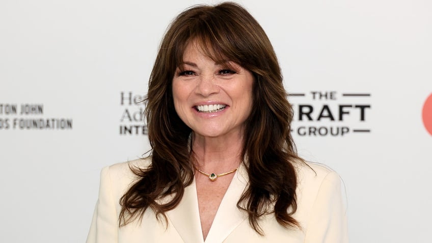 Valerie Bertinelli smiling in a cream suit with a white background