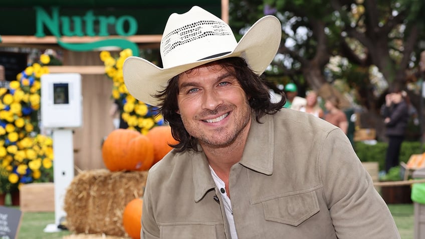 Ian Somerhalder in a tan jacket and cream cowboy hat smiles at the camera