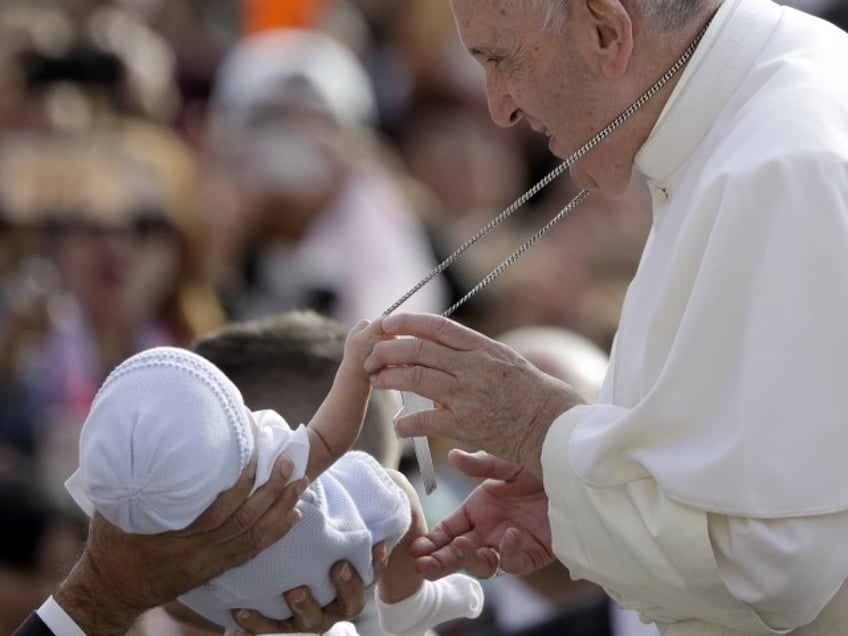 A baby handed over to Pope Francis to bless grabs onto his cross as he arrives for his weekly general audience in St. Peter's Square, at the Vatican, Wednesday, Sept. 25, 2019.