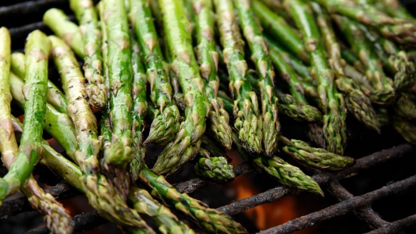 A bunch of fresh asparagus sits on a grill.