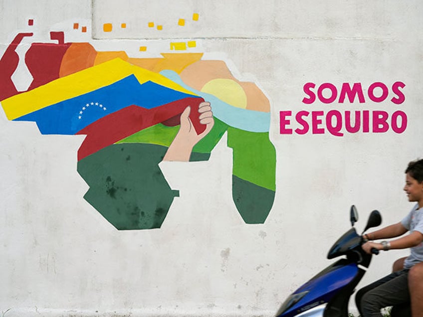 A youth drives a motorcycle in front of a mural of a map of Venezuela with the Essequibo t