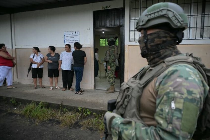 Military personnel stand guard as women queue to vote at a polling station in Canuto, Ecua