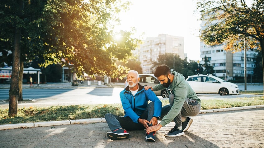 Son helping his father to stand up after his fall while jogging outdoors