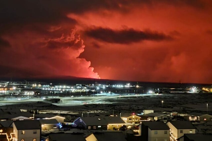 Houses in Iceland's Hafnarfjordur are seen as smoke billows in the distance, the night sky turned orange by lava from an volcanic eruption