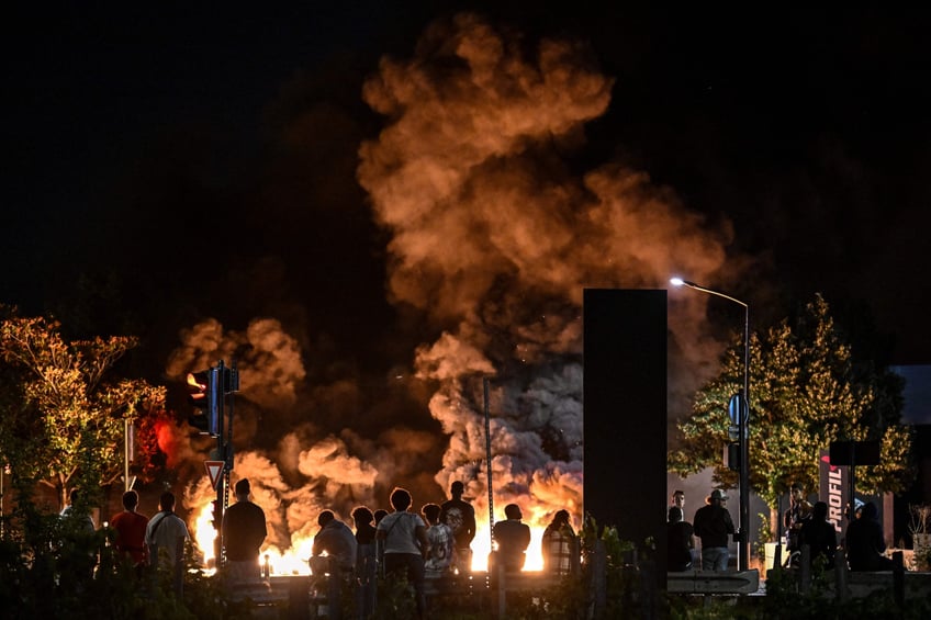 TOPSHOT - People look at burning tyres blocking a street in Bordeaux, south-western France on late June 29, 2023, during riots and incidents nationwide after the killing of a 17-year-old boy by a police officer's gunshot following a refusal to comply in a western suburb of Paris. (Photo by Philippe LOPEZ / AFP) (Photo by PHILIPPE LOPEZ/AFP via Getty Images)