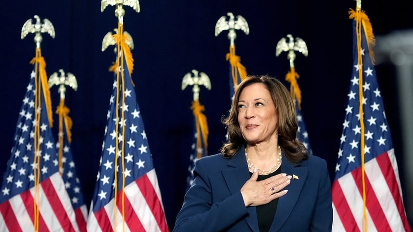 Kamala Harris with hand on heart, US flags behind her