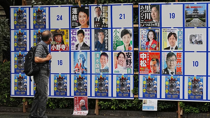 A man on the street looks at a billboard covered with campaign advertisements for Tokyo gubernatorial candidates.