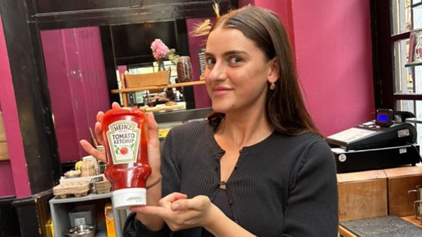 Brunette woman smiling and holding a bottle of ketchup.