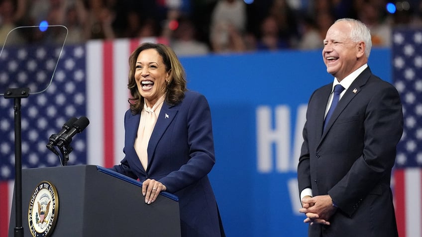 Kamala Harris laughing at lectern, Tim Walz behind her to her left