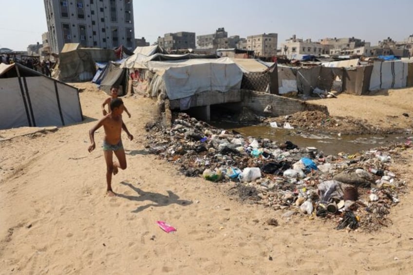 Children play next to garbage and sewage at a camp for displaced Palestinians in Deir el-B