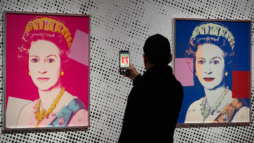 A man takes an image of a Warhol portrait depicting Queen Elizabeth II