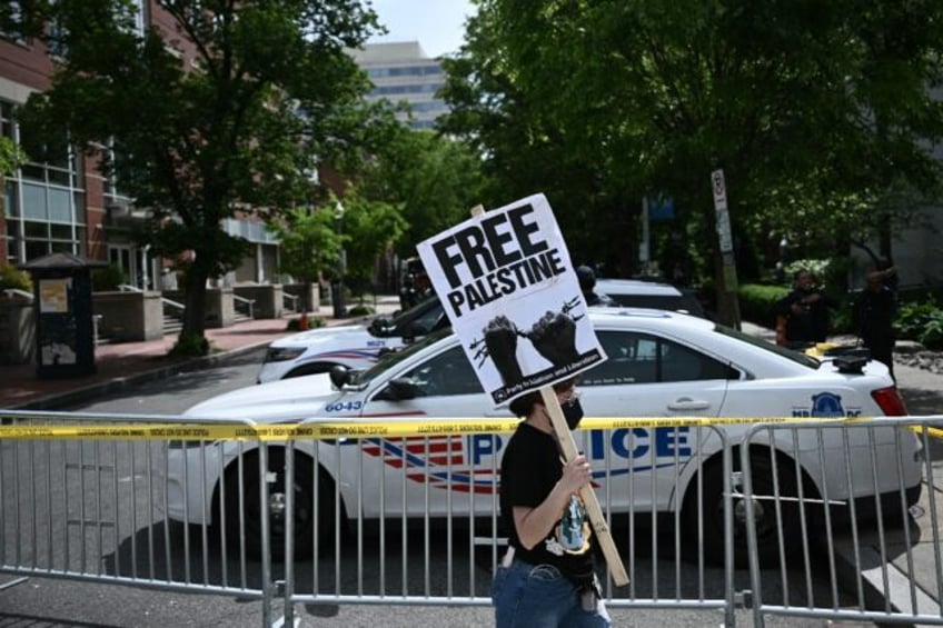 A demonstrator holds a sign as a police vehicle and barricades block a road after officers