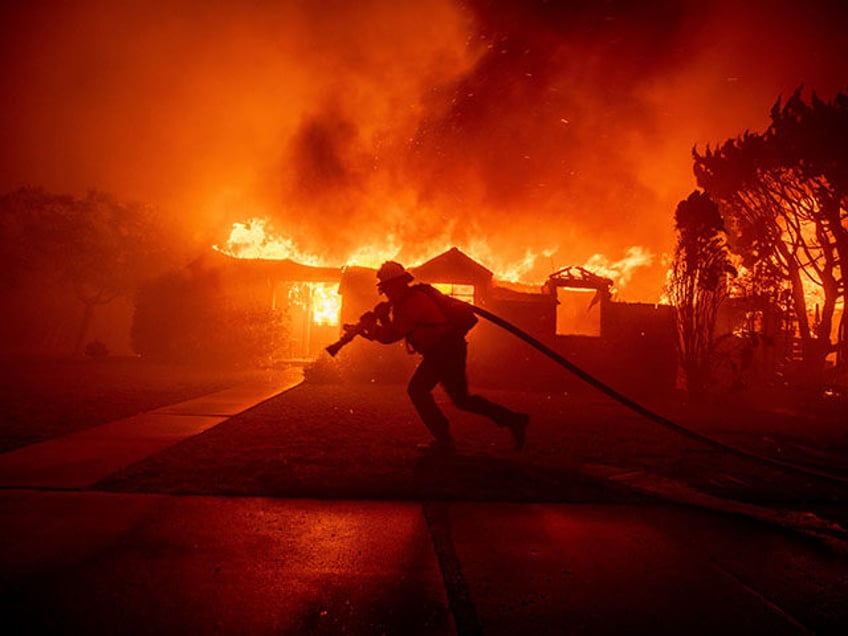 A firefighter battles the Palisades Fire as it burns a structure in the Pacific Palisades