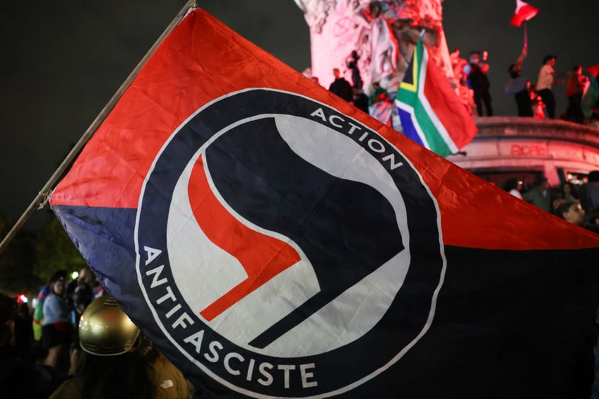 An "Antifascist action flag" is seen during an election night rally following the first results of the second round of France's legislative election at Place de la Republique in Paris on July 7, 2024. A loose alliance of French left-wing parties thrown together for snap elections was on course to become the biggest parliamentary bloc and beat the far right, according to shock projected results. (Photo by EMMANUEL DUNAND / AFP) (Photo by EMMANUEL DUNAND/AFP via Getty Images)