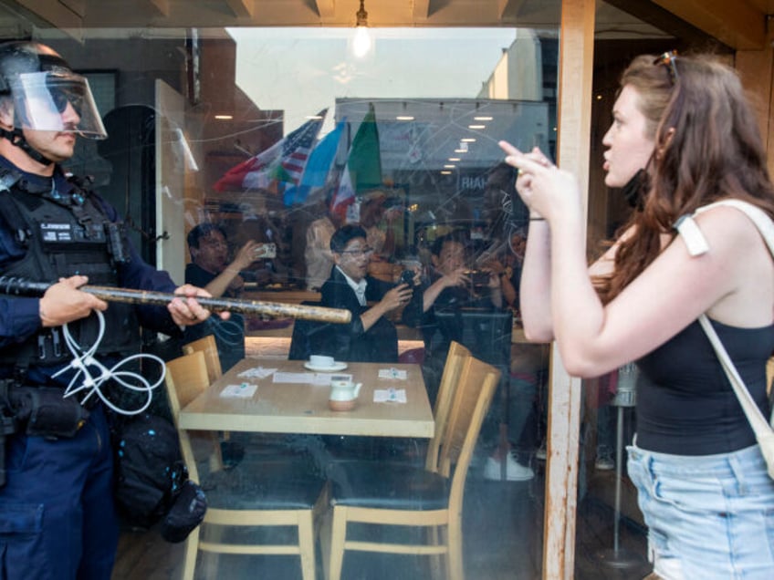 Diners in a restaurant look on as a protester gestures toward a police officer in riot dur