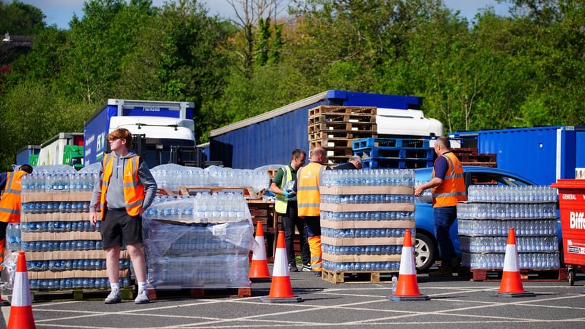 Workers in orange vests stand around pallets full of bottled water so people at Broadsands Car Park in Paignton, England