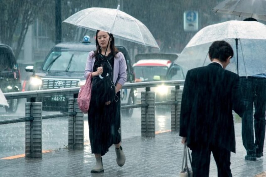 People carrying umbrellas walk across a street in Tokyo on August 30. Typhoon Shanshan wea