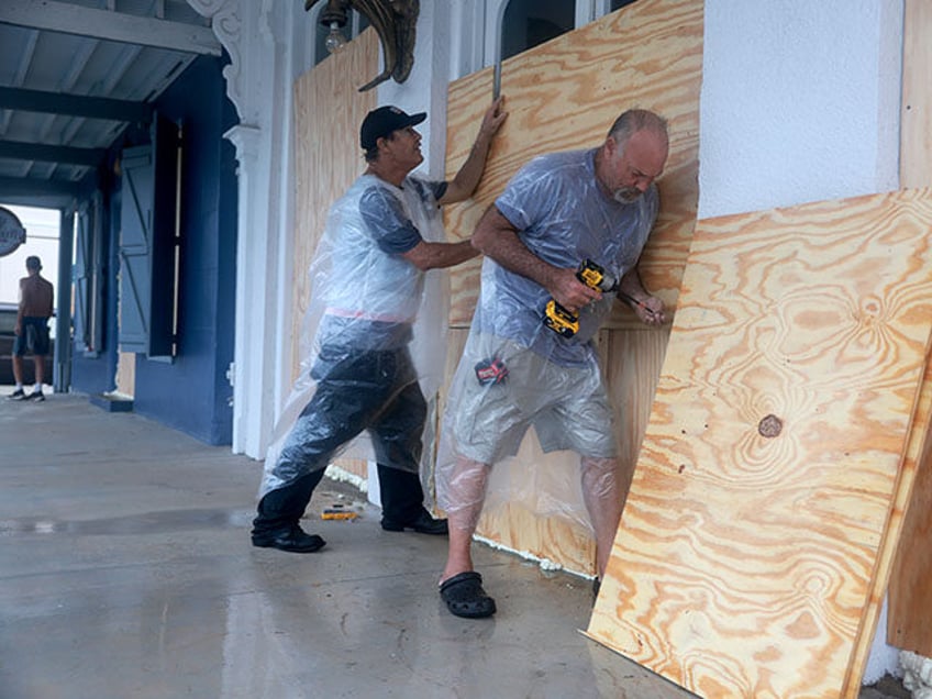 Tom Street (L) and Dan Norman place plywood over the windows of a business as they prepare