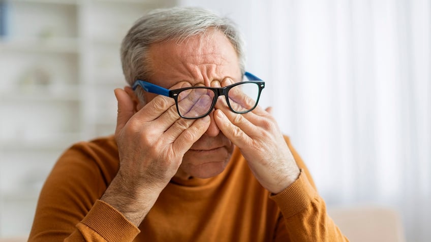 elderly man rubbing eyes under eyeglasses