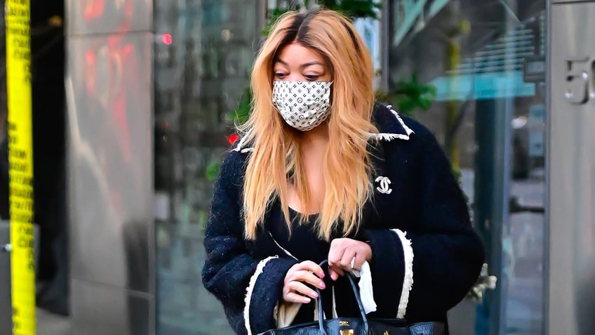 Wendy Williams looks down wearing a mask in a black jacket