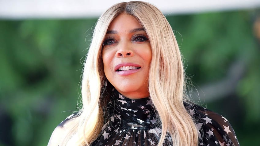 Wendy Williams in a black patterned top looks up slightly and smiles