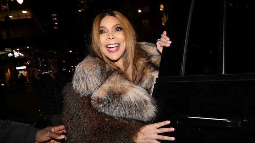 Wendy Williams in a brown coat with fur trim smiles as she gets into a car in New York City