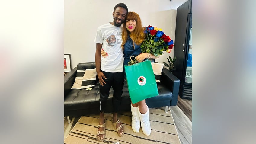 Wendy Williams smiles in a blue outfit poses with owner of shop holding a teal bag and wearing white moon boots