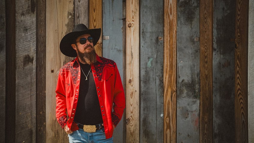 Whey Jennings wearing a red jack and standing in front of a grey and wood fence.