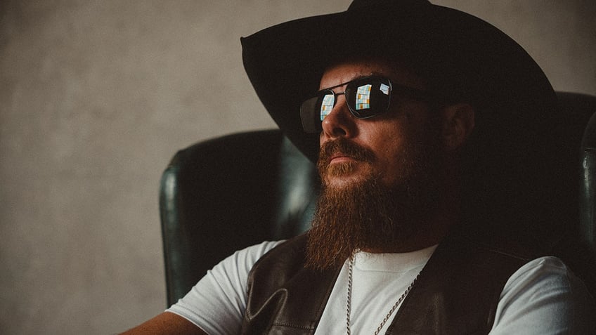 Whey Jennings wearing a white shirt, a vest and sunglasses with a cowboy hat