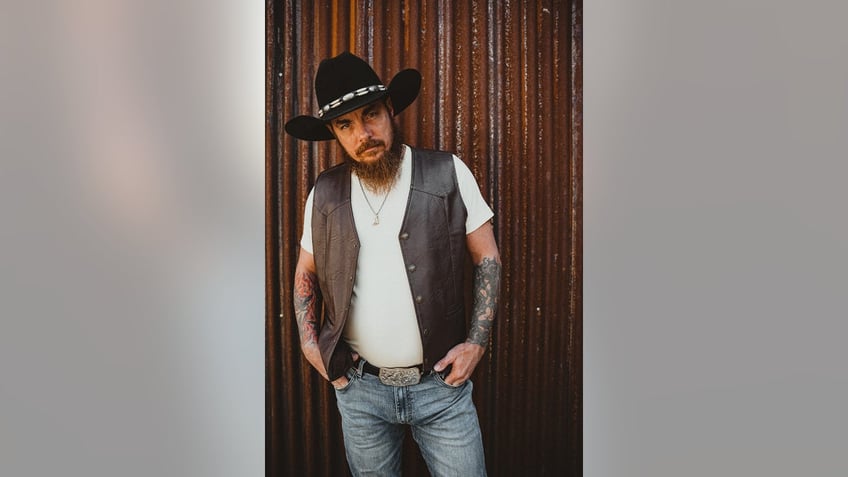 Whey Jennings wearing a white shirt and a vest with jeans and a cowboy hat.