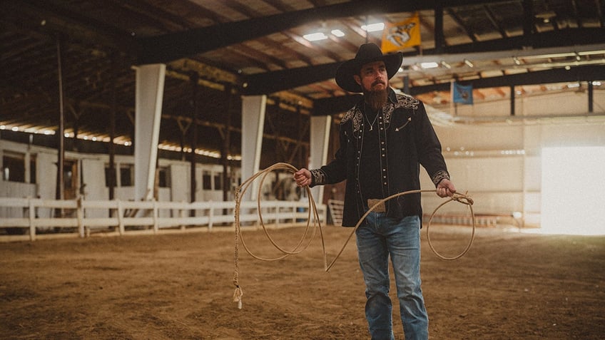 Whey Jennings holding a rope and wearing a black shirt with blue jeans