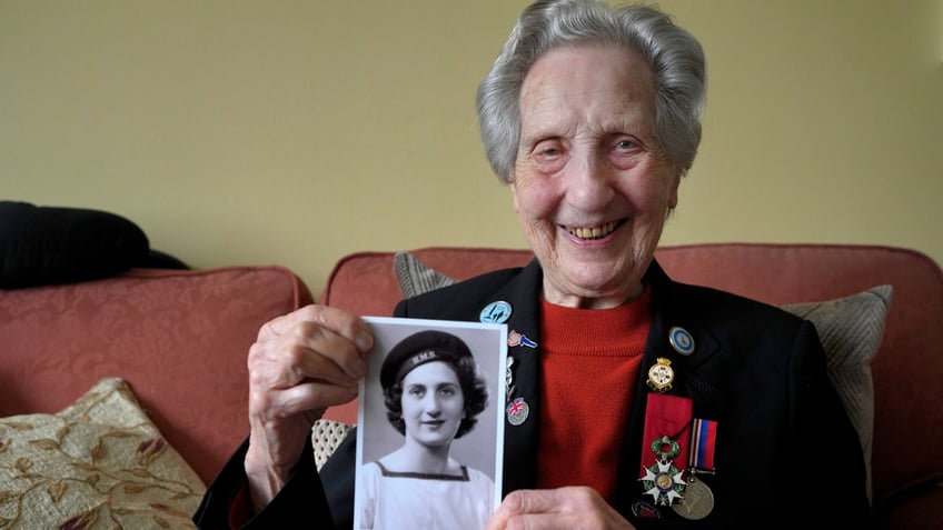 Marie Scott who was a serving Wren and switchboard operator at the time of D-Day, holds up a photograph of herself in 1944, at her home in London.