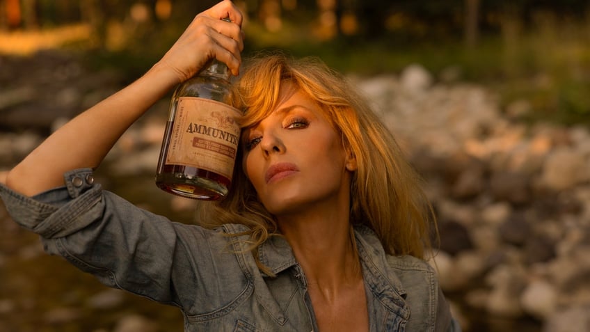 "Yellowstone" actress Kelly Reilly presses a bottle of Ammunition whiskey against her head during a photography session for the California-based whiskey and winemaker.