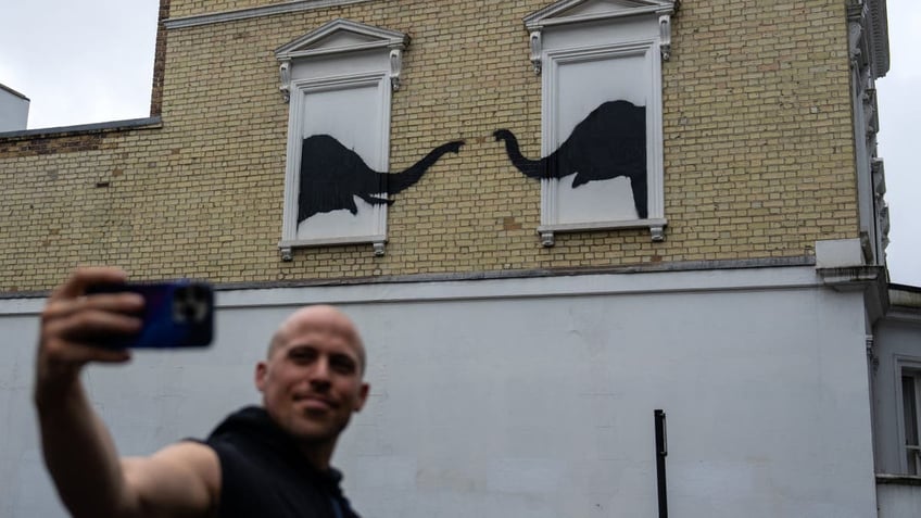 Man taking selfie in front of Banksy art