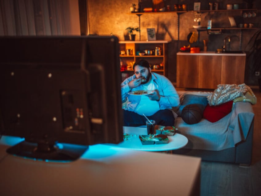 Overweight man eating fast food and drinking soda while sitting on sofa and watching baske