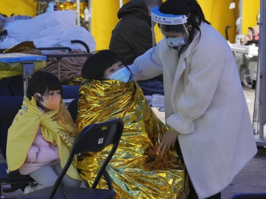 A woman with children wearing face masks wait at a temporary makeshift treatment area outside Caritas Medical Centre in Hong Kong, Friday, Feb. 18, 2022. Hong Kong's hospitals reached 90% capacity on Thursday and quarantine facilities were at their limit, authorities said, as the city struggles to snuff out a record number of new COVID-19 cases by adhering to China's "zero tolerance" strategy.