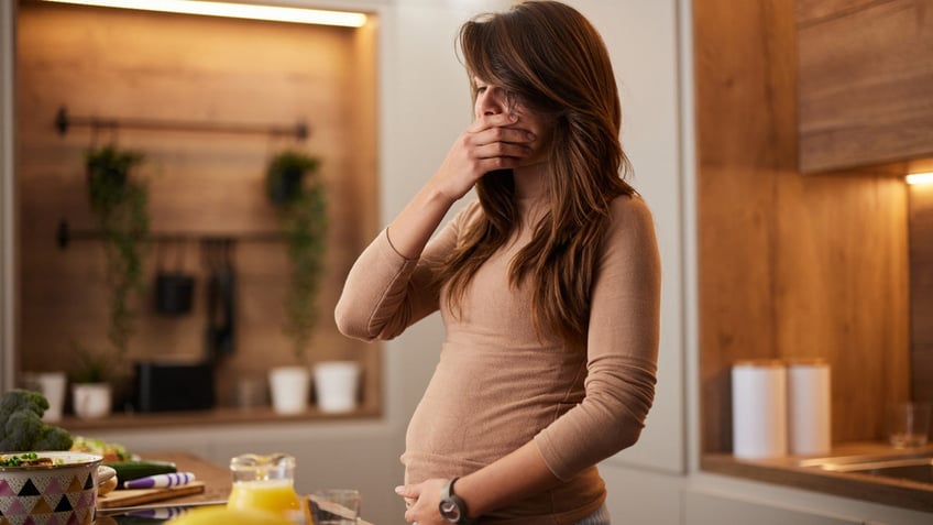 Young pregnant woman covering her mouth while food in the kitchen is making her sick.