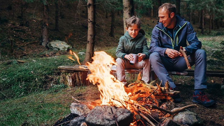 father and son sit near a campfire