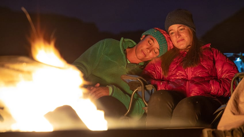 two women sit close to eachother in front of a fire
