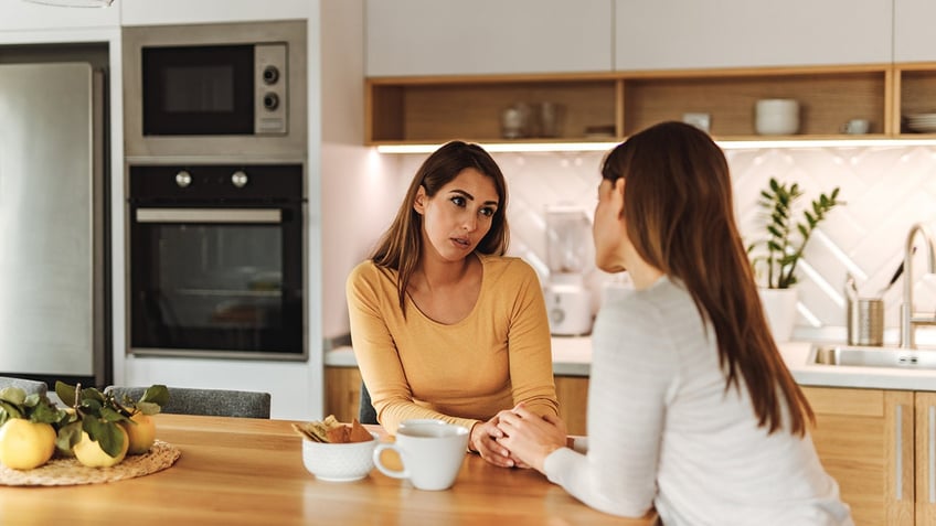 Two women talking in a kitchen setting.