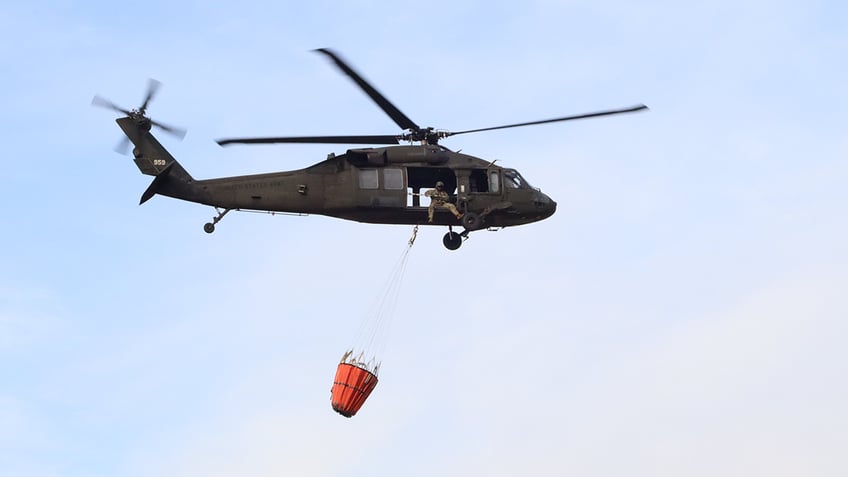 An orange water bucket hangs below a Black Hawk helicopter