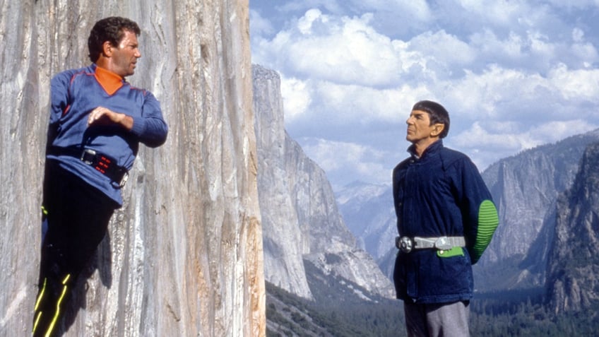William Shatner as Kirk in his blue outfit leans against a rock oppposite Leonard Nimoy as Spock in "Star Trek V: The FInal Frontier"