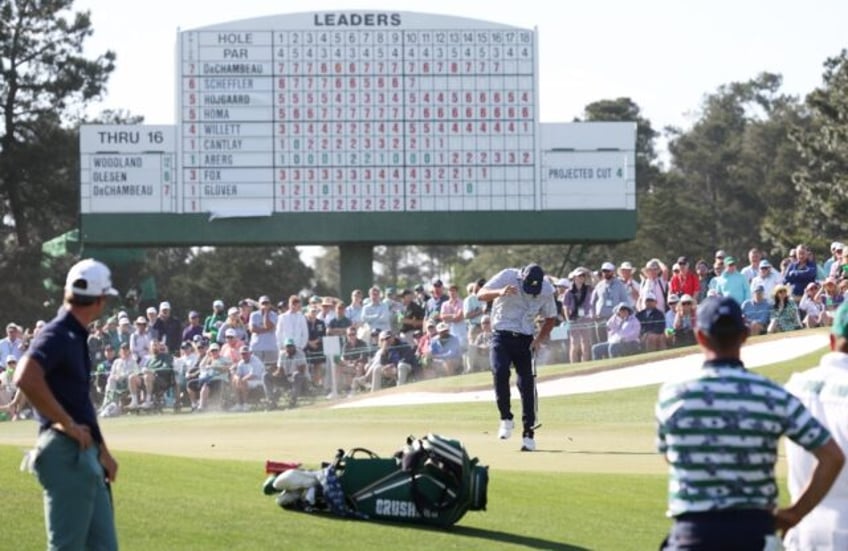 Bryson DeChambeau of the United States shields himself from the wind, blowing sand, on the