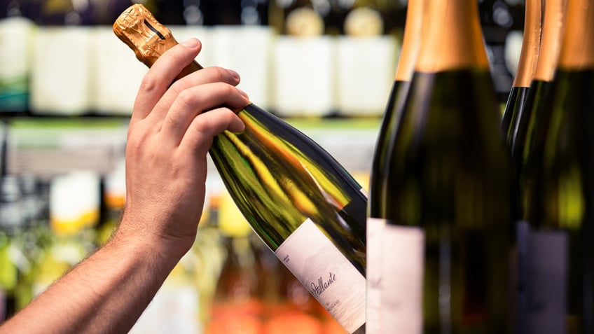 A hand selects a bottle of sparking wine from a store shelf.